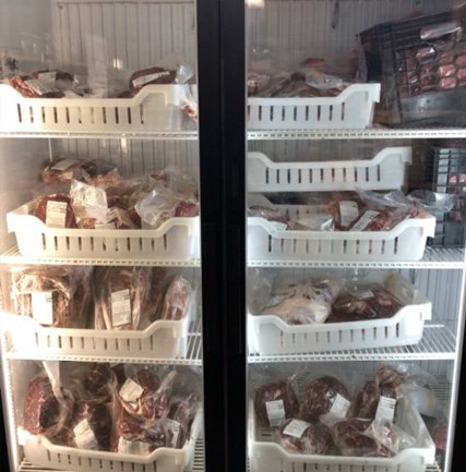 Meat display refrigerator showcasing various packaged cuts of beef and pork neatly organized in plastic bins, highlighting a variety of meat options for consumers.