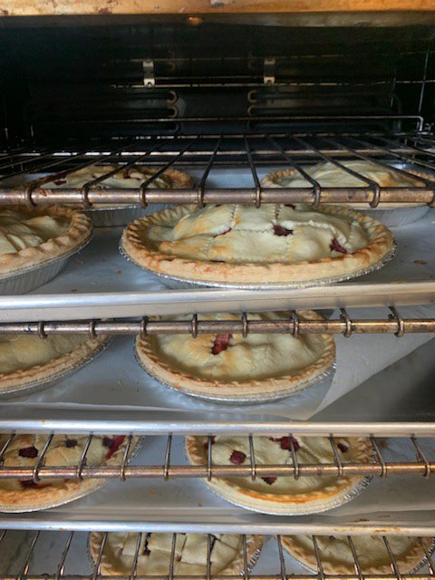 img-0204 (1) Baking pies in an oven with multiple racks, showcasing several fruit-filled pies cooling on the middle and lower shelves, highlighting the golden crusts and delicious fillings.