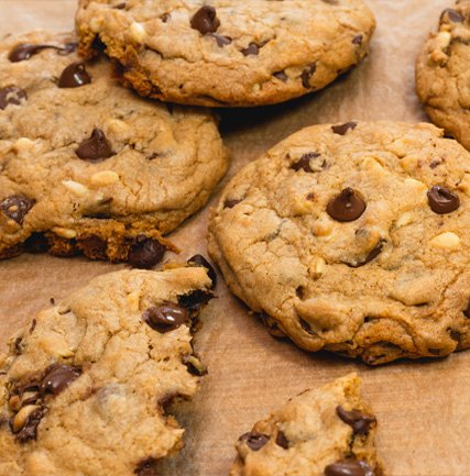 img-0211 (1) Freshly baked chocolate chip cookies on parchment paper, showcasing a variety of sizes and textures with melted chocolate chips and a golden-brown color. Perfect for dessert or a sweet snack.