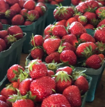 Freshly picked strawberries in green containers, showcasing their vibrant red color and green leafy tops, arranged neatly for sale at a farmers market.