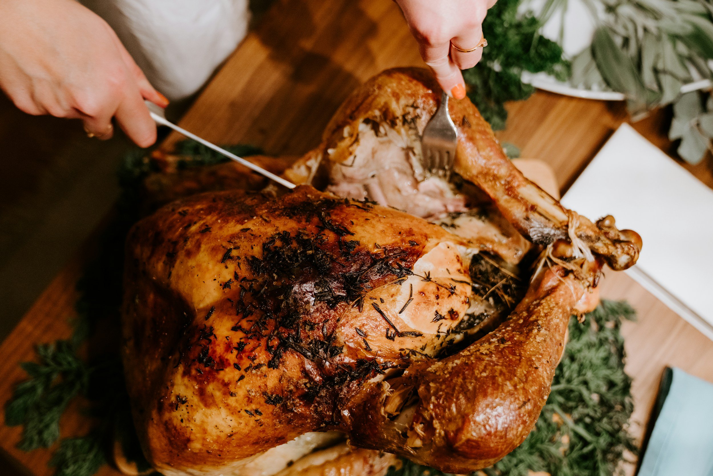 unsplash-image-cgcteFH-azk (1) A close-up of a beautifully roasted turkey being carved, showcasing golden-brown skin, herbs, and garnishes on a wooden serving board. The image captures the process of preparing a festive meal, ideal for Thanksgiving or holiday gatherings.